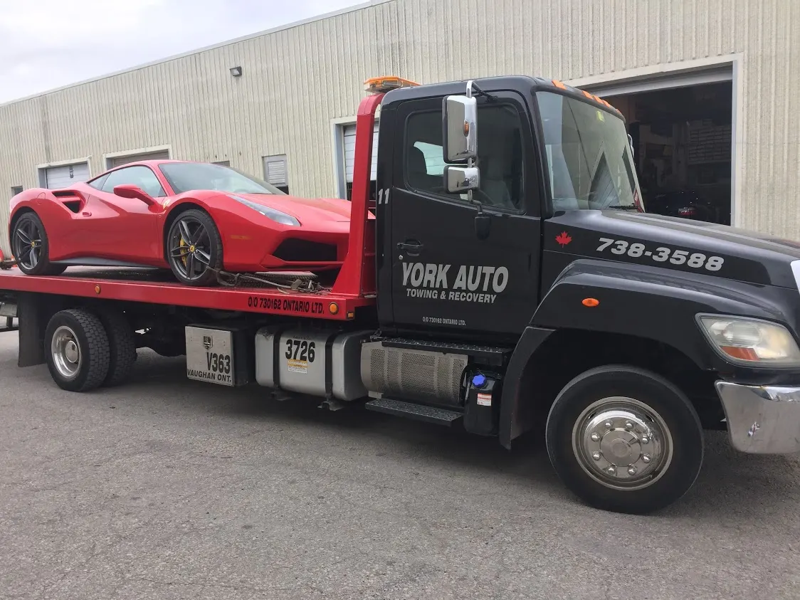A York Auto flatbed tow truck carrying a red sports car